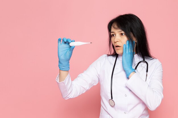 Mujer joven en traje médico blanco guantes azules con estetoscopio en rosa