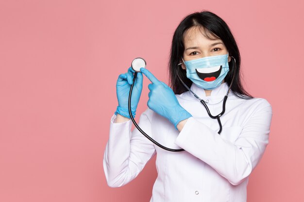 mujer joven en traje médico blanco guantes azules máscara protectora azul con estetoscopio en rosa