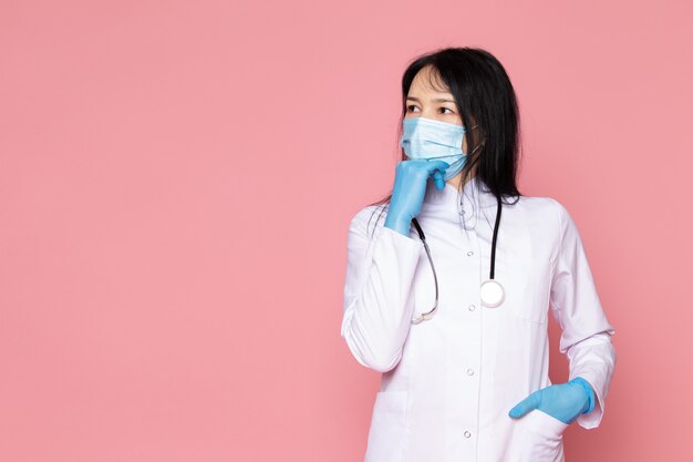 mujer joven en traje médico blanco guantes azules máscara protectora azul con estetoscopio en rosa