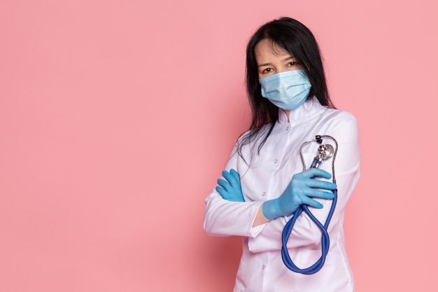 mujer joven en traje médico blanco guantes azules máscara protectora azul con estetoscopio en rosa