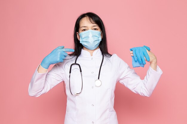 mujer joven en traje médico blanco guantes azules máscara protectora azul con estetoscopio en rosa