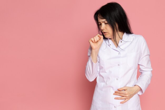 mujer joven en traje médico blanco tosiendo en rosa