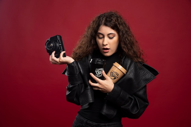 Mujer joven en traje negro sosteniendo una taza y una cámara.