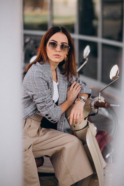 Mujer joven en traje de pie junto a la moto