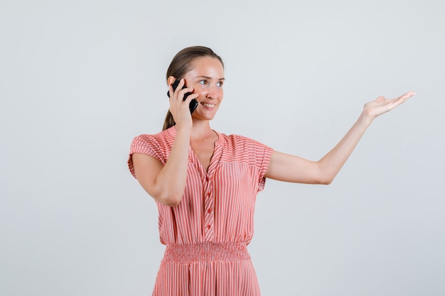 Foto gratuita mujer joven en traje de rayas hablando por teléfono con la palma de la mano a un lado, vista frontal.