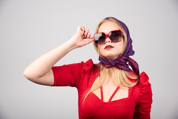 Mujer joven en traje rojo posando sobre fondo gris.