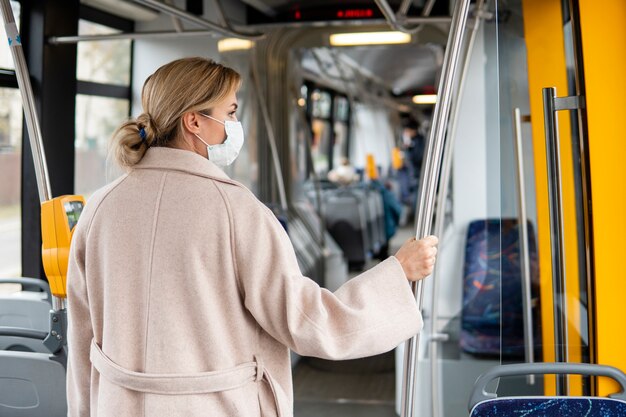 Mujer joven con transporte público con mascarilla quirúrgica