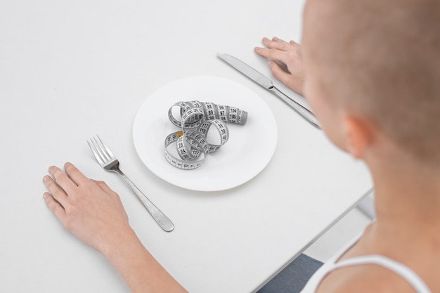 Foto gratuita mujer joven con un trastorno alimentario con una cinta métrica en el plato