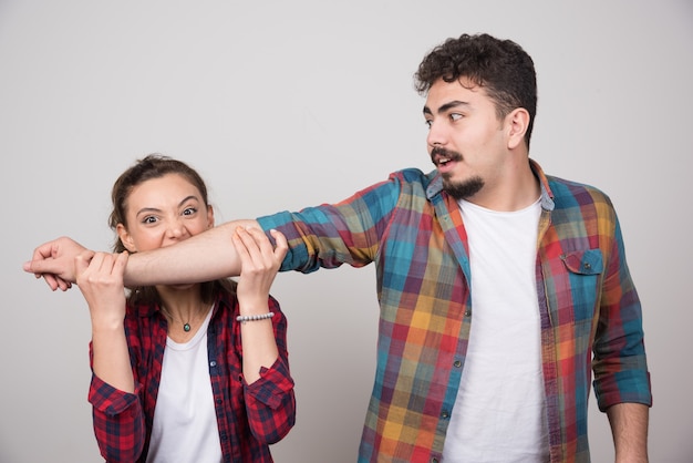 Mujer joven tratando de morder la mano del hombre en una pared gris.