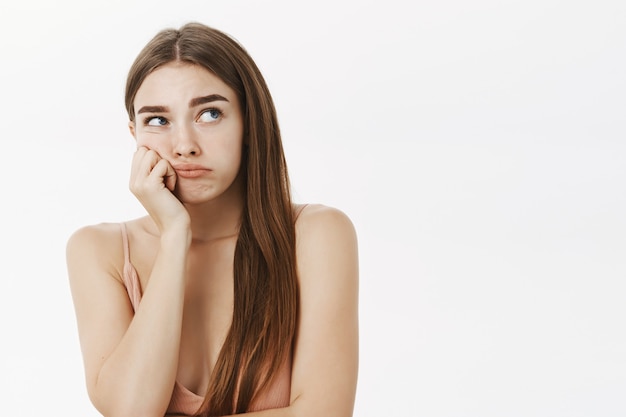 Mujer joven triste y malhumorada con un hermoso cabello largo y castaño, apoyando la cabeza en la mano y mirando con tristeza e indiferencia la esquina superior derecha como si se sintiera celoso