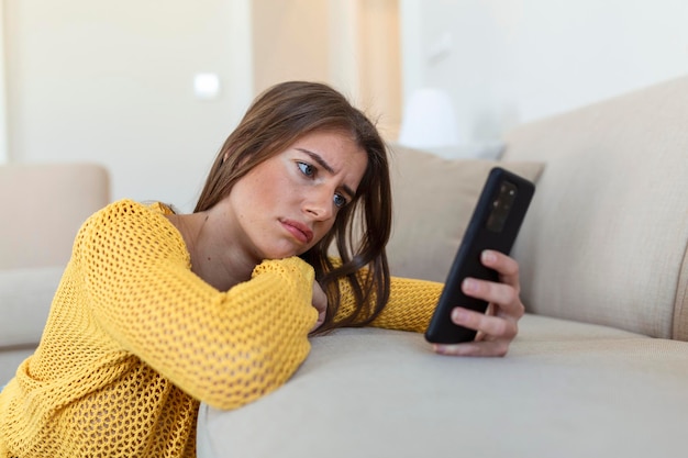 Mujer joven triste y pensativa sosteniendo un teléfono inteligente esperando sms de su novio