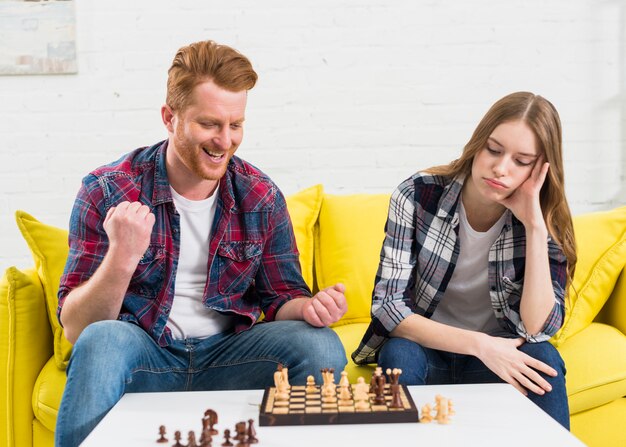 Mujer joven triste que se sienta con su novio que anima después de ganar el juego de ajedrez en casa