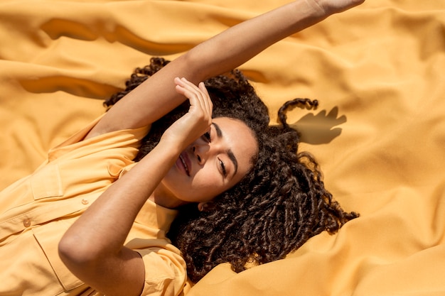 Foto gratuita mujer joven tumbada en tela amarilla en la naturaleza