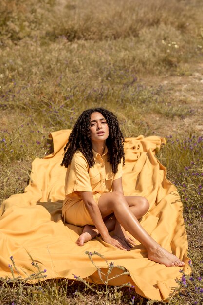 Mujer joven tumbada en tela amarilla en la naturaleza