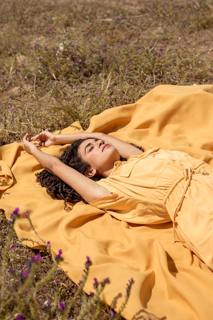 Foto gratuita mujer joven tumbada en tela amarilla en la naturaleza