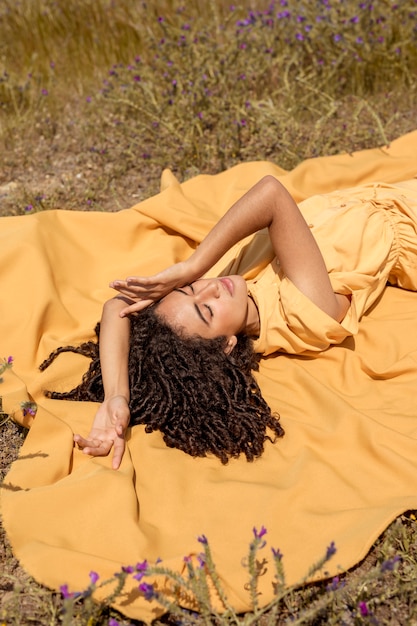 Foto gratuita mujer joven tumbada en tela amarilla en la naturaleza