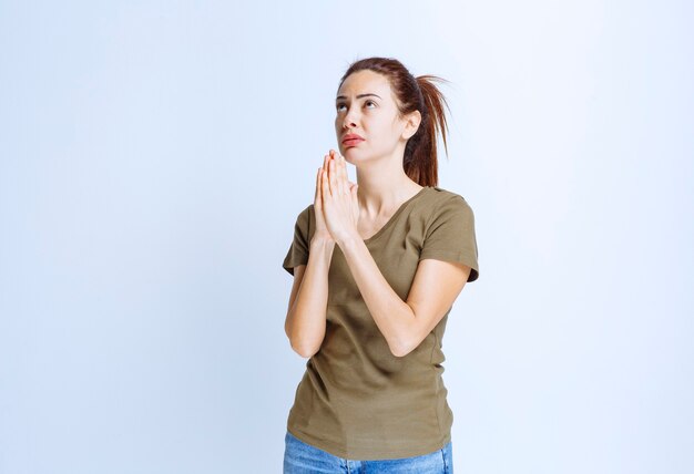 Mujer joven uniendo sus manos y soñando o rezando