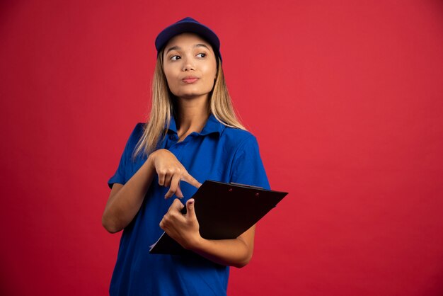 Mujer joven en uniforme azul apuntando al portapapeles.