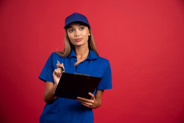 Mujer joven en uniforme azul posando con lápiz y portapapeles.