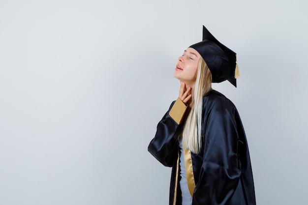 Mujer joven en uniforme graduado examinando la piel de su cuello y luciendo delicada.