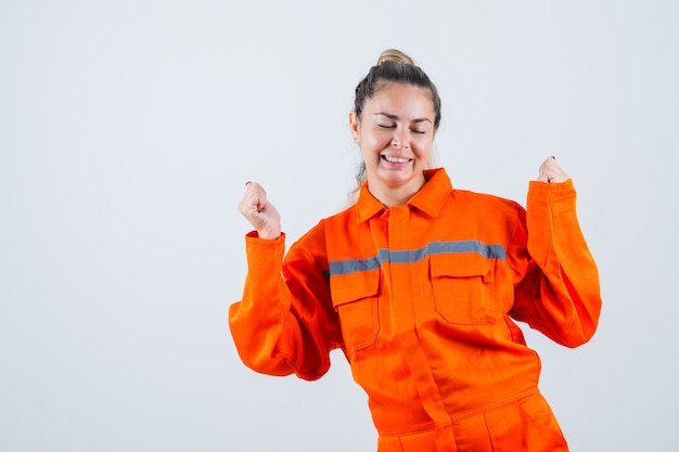 Mujer joven en uniforme de trabajador mostrando gesto de ganador y mirando satisfecho, vista frontal.