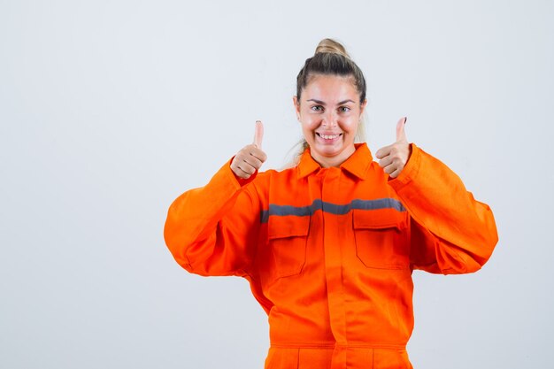 Mujer joven en uniforme de trabajador mostrando el pulgar hacia arriba y mirando contento, vista frontal.