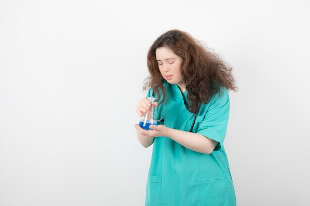 mujer joven en uniforme verde sosteniendo un frasco de vidrio con líquido azul.