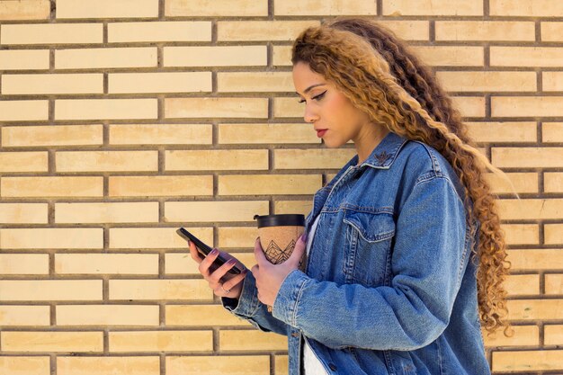 Mujer joven urbana con smartphone enfrente de muro de ladrillo