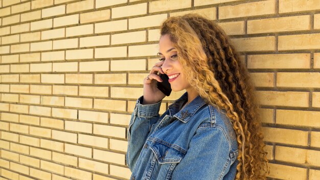 Mujer joven urbana con smartphone enfrente de muro de ladrillo