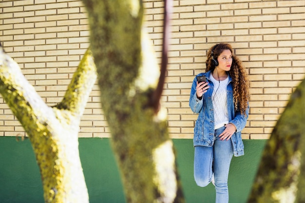 Foto gratuita mujer joven urbana con smartphone enfrente de muro de ladrillo