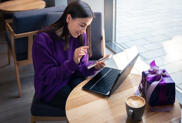 Mujer joven usa teléfono inteligente y computadora portátil en concepto de vacaciones de café