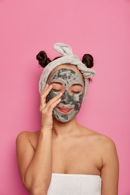 Mujer joven usa tratamientos para la piel de mascarilla de arcilla facial natural después de tomar un baño