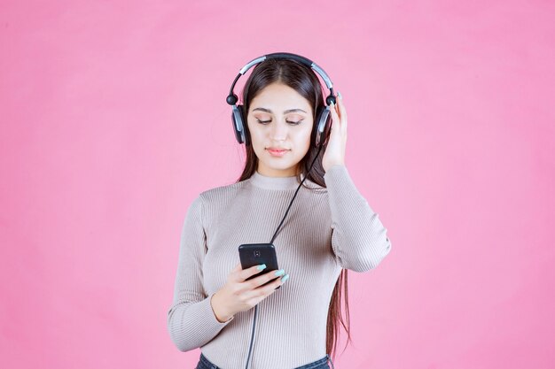 Mujer joven usando audífonos y poniendo música en su teléfono inteligente