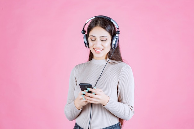 Mujer joven usando audífonos y poniendo música en su teléfono inteligente