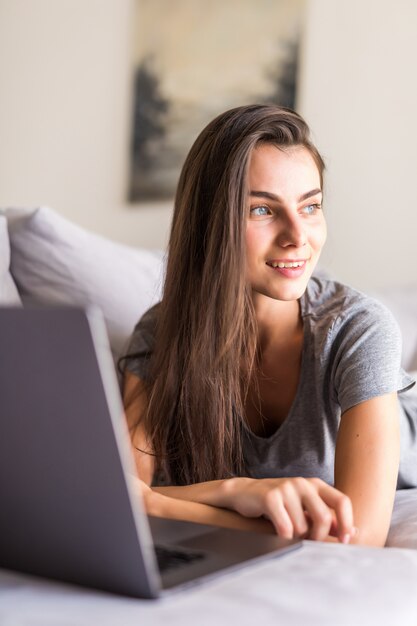 Mujer joven usando una computadora portátil mientras se relaja en el sofá