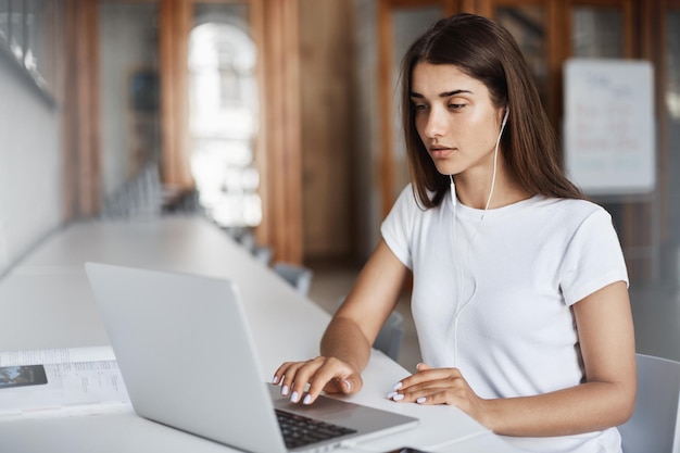 Mujer joven usando una computadora portátil viendo películas en tiempo real o escuchando música en línea en el campus universitario