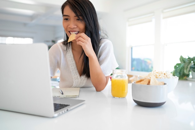 Mujer joven usando laptop y comiendo chips de tortilla