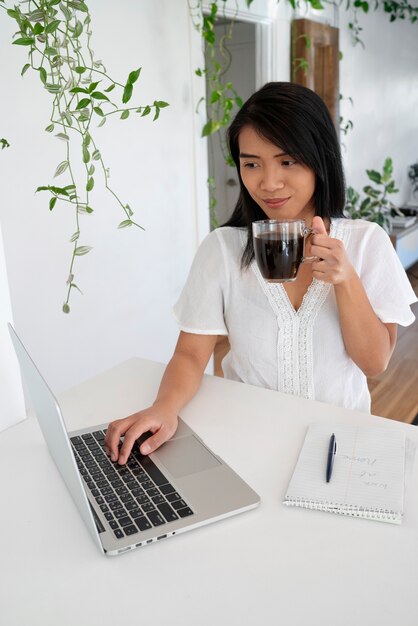 Mujer joven usando laptop y tomando una taza de café