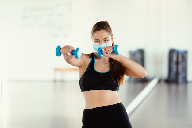Mujer joven usar máscara y hacer ejercicios con pesas