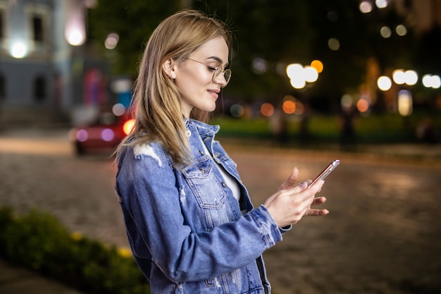 Mujer joven usar teléfono móvil en la ciudad de noche