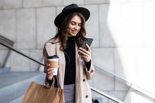 Mujer joven uso de teléfono móvil y sosteniendo la bolsa de compras en la calle