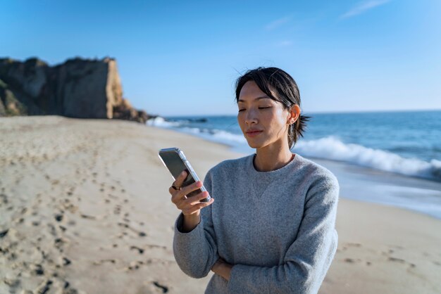 mujer joven, utilizar, teléfono inteligente, en la playa