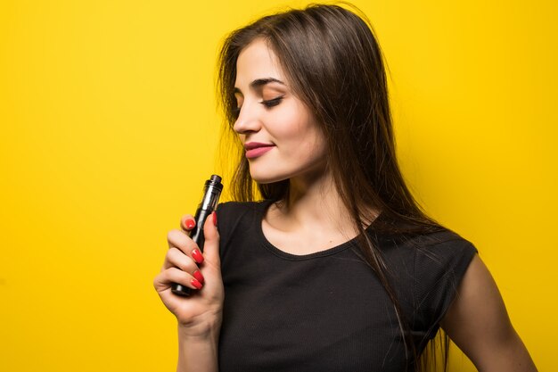 Mujer joven con vape humo gadget de pie en la pared amarilla