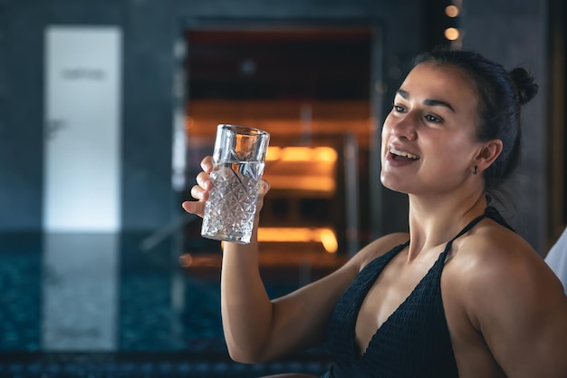 Una mujer joven con un vaso de agua después de la sauna descansa