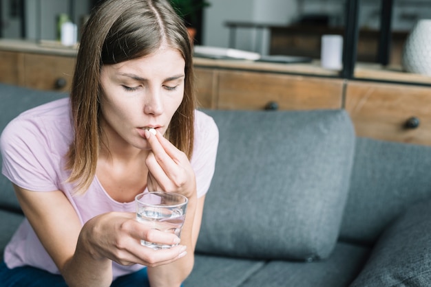 Mujer joven con vaso de agua tomando medicina