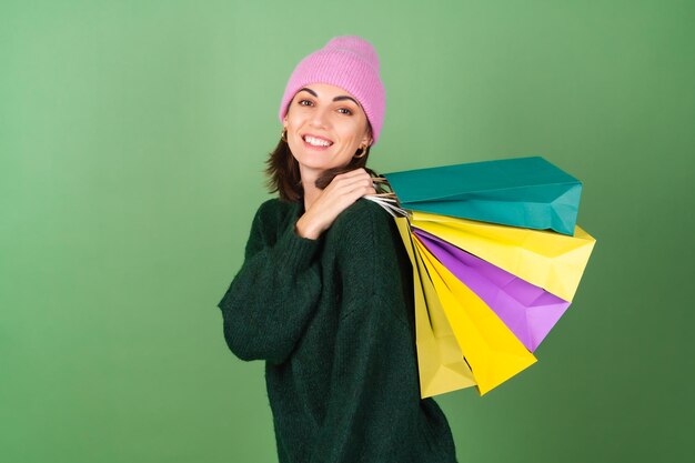 Mujer joven en verde en un cálido suéter acogedor y un sombrero rosa con bolsas de colores