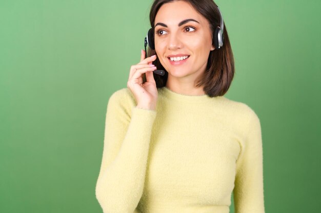 Mujer joven en verde en un suéter amarillo gerente, trabajador de servicio de apoyo, vendedor, acepta con placer llamadas de clientes