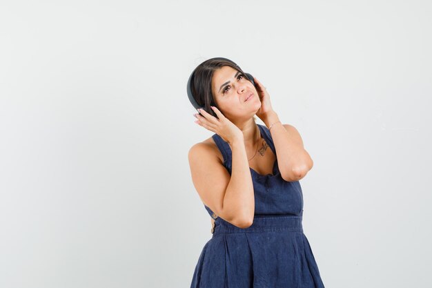 Mujer joven vestida disfrutando de la música con auriculares y mirando soñadora