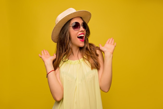 Mujer joven en vestido amarillo con sombrero y gafas de sol