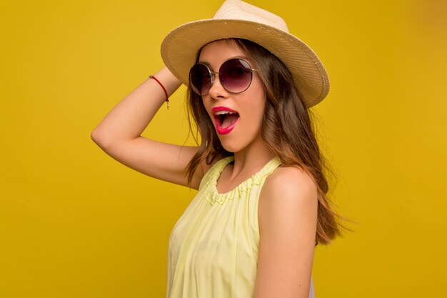 Mujer joven en vestido amarillo con sombrero y gafas de sol